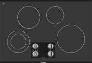 Black seamless glass electric cooktop with four burners and front control knobs in Bosch kitchen appliances collection