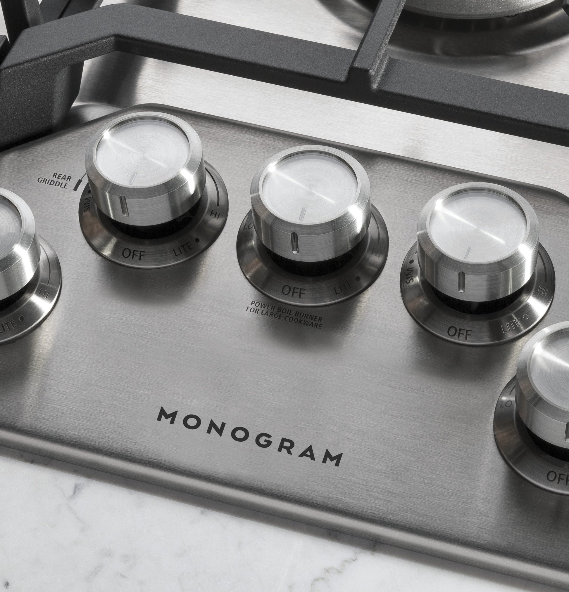 Close-up of stainless steel gas cooktop control knobs with Monogram branding for kitchen appliances collection