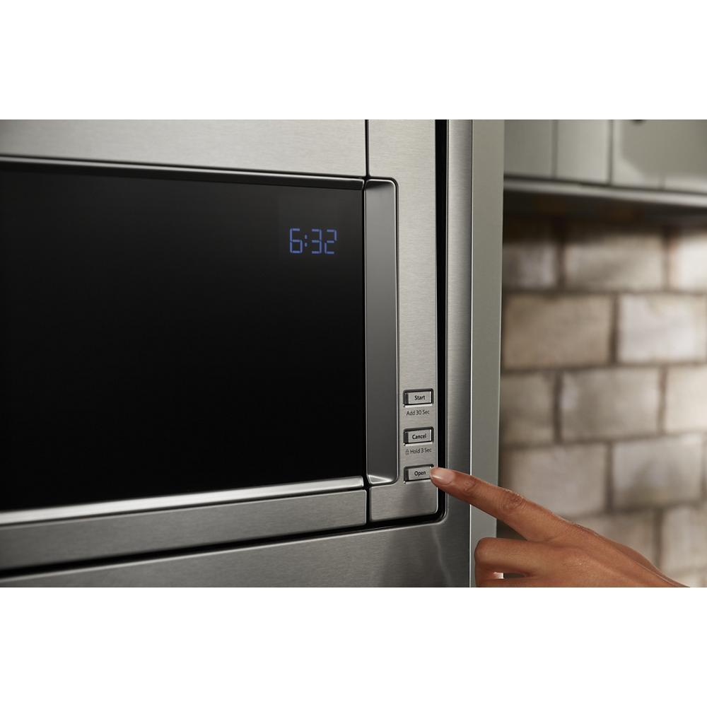 Close-up of stainless steel built-in microwave digital control panel with finger pressing open button in modern kitchen