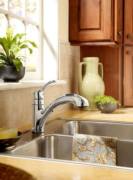 Chrome single-handle low arc pullout kitchen faucet installed on a countertop with double stainless steel sinks and wooden cabinets nearby