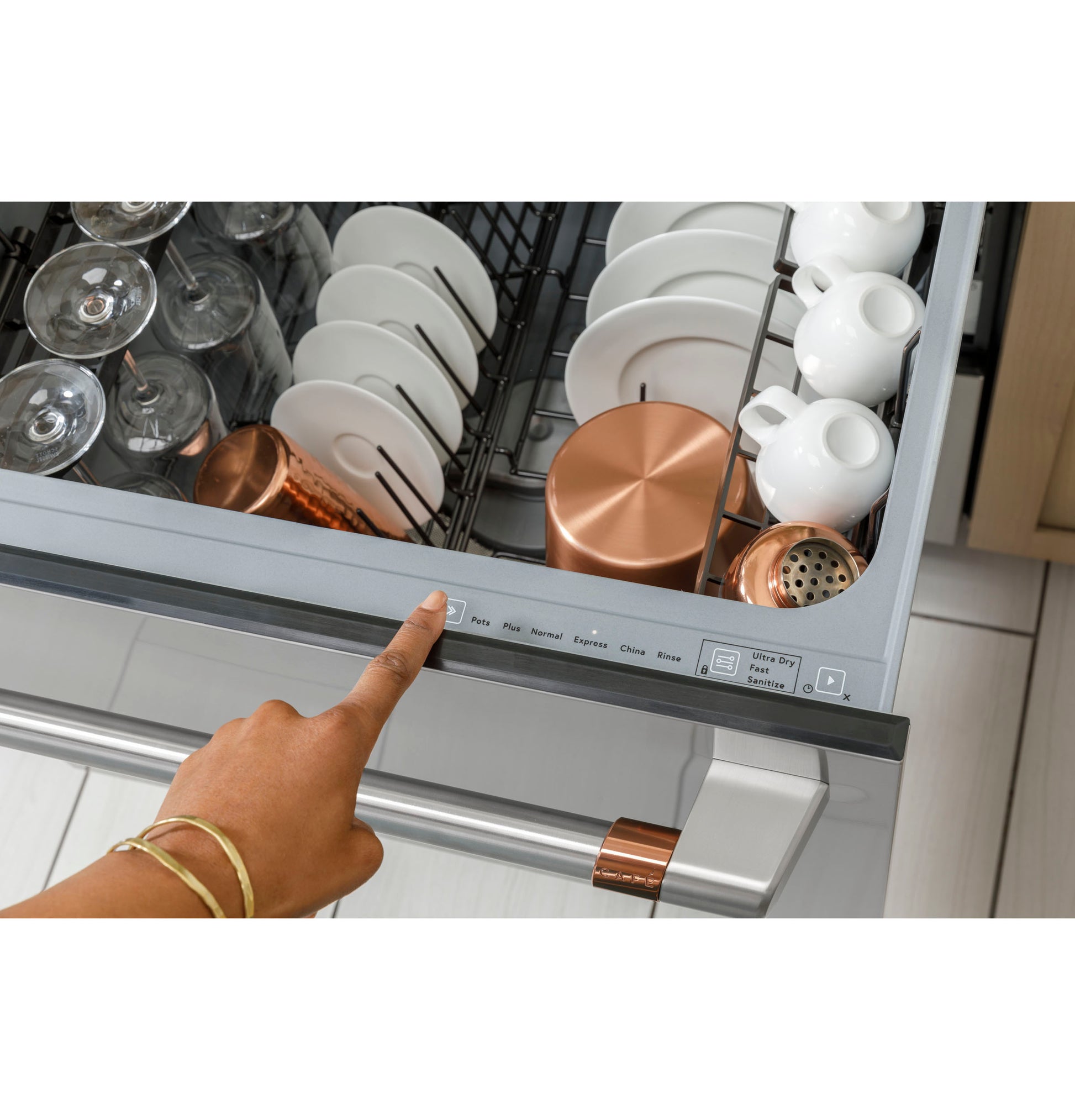 Hand pressing control button on stainless steel dishwasher drawer loaded with dishes and glassware in modern kitchen
