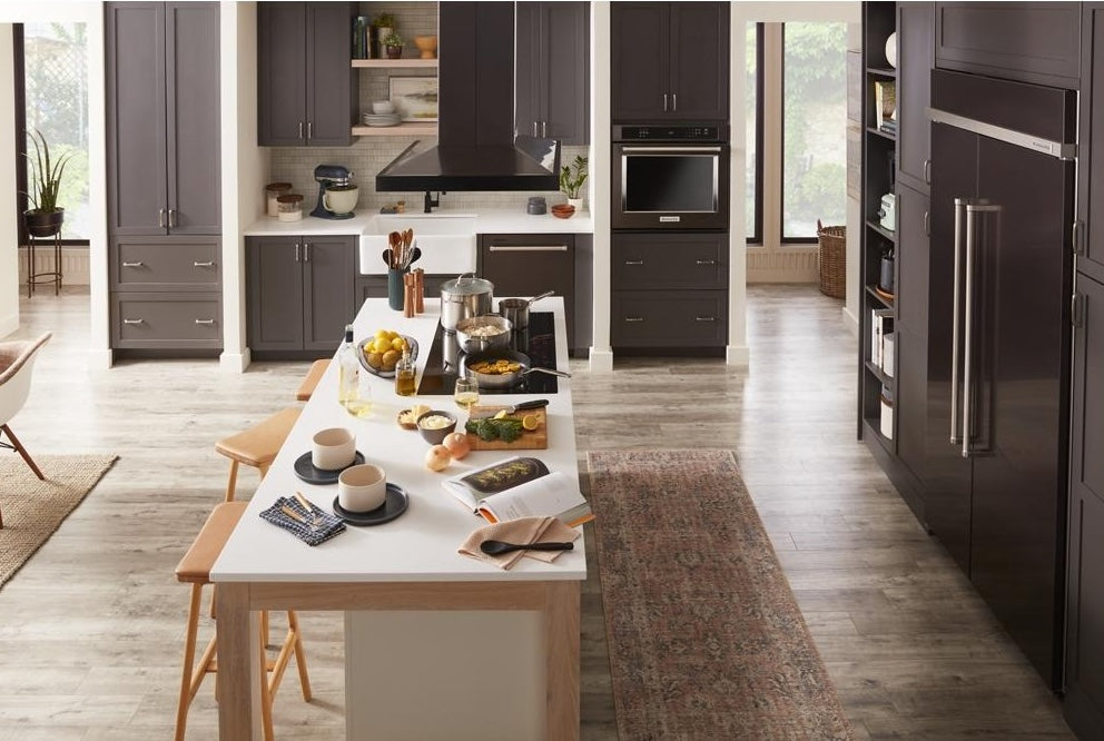 Contemporary kitchen featuring a modern island with cooking utensils, a sleek island-mount canopy hood, and matching dark cabinetry, part of Island Range Hoods and Kitchen & Kitchenware collections.