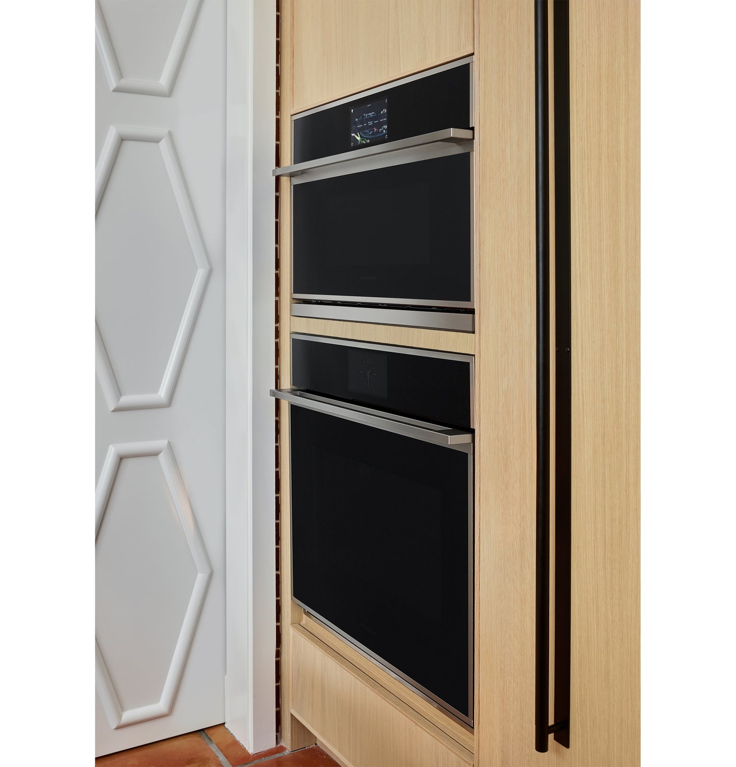 Minimalist five-in-one wall oven with black glass and stainless steel trim integrated into light wood cabinetry in kitchen setting