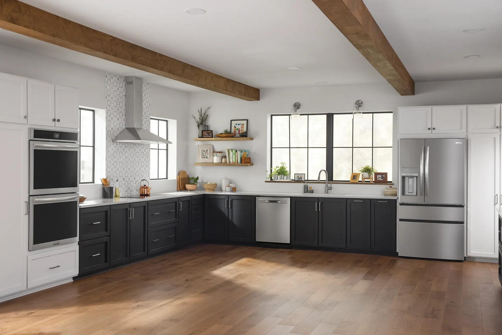 Modern spacious kitchen with black lower cabinets, white upper cabinetry, stainless steel appliances, and wood ceiling beams