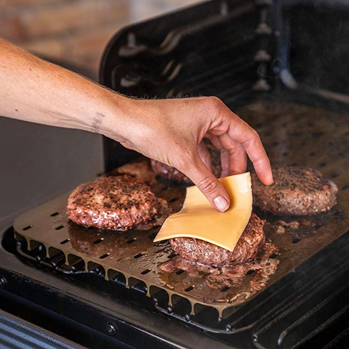 Hand placing cheese slice on burger patty cooking on anodized aluminum sear gate in grilling accessories collection