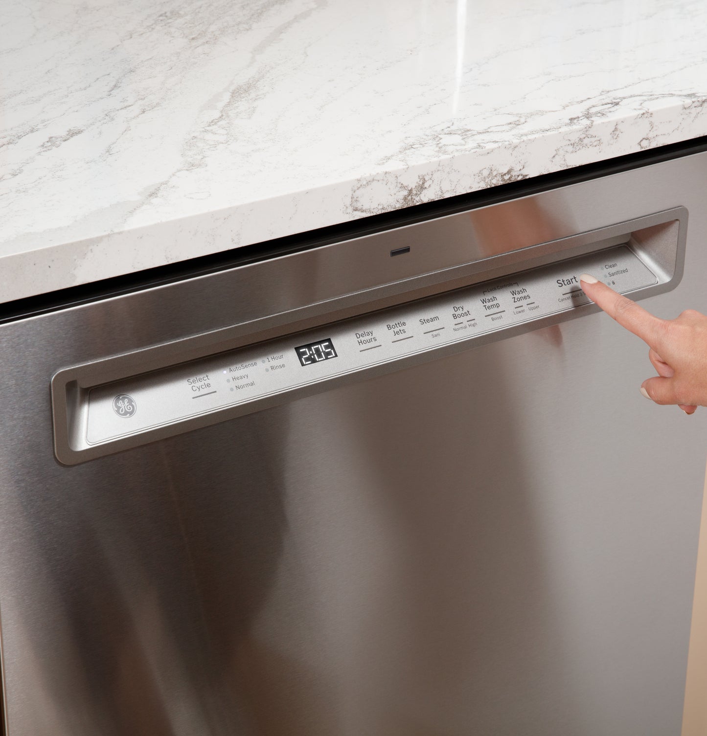 Finger pressing start button on stainless steel front control dishwasher integrated under marble countertop in kitchen
