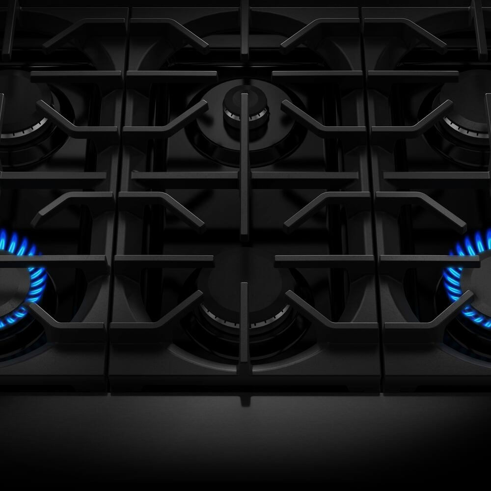 Black gas cooktop with six burners and blue flames under cast iron grates in a modern kitchen appliance setting