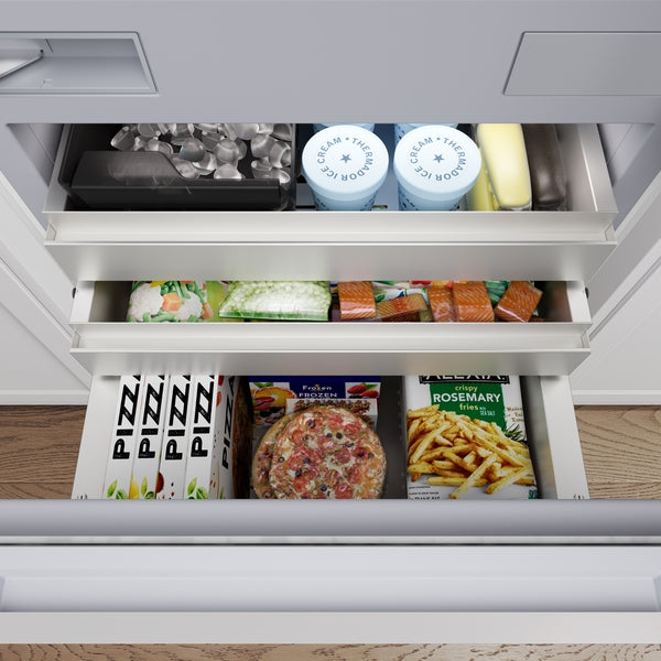 Open built-in bottom freezer drawer with ice, frozen fish fillets, pizzas, and crispy fries from Thermador appliances collection