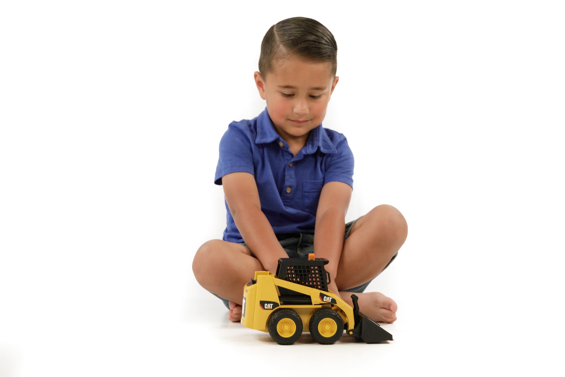 Young child in blue shirt playing with a yellow Bruder CAT skid steer loader toy for imaginative home improvement play