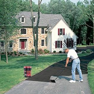 Man applying black asphalt resurfacing filler and sealer from 5-gallon container on driveway in home improvement setting