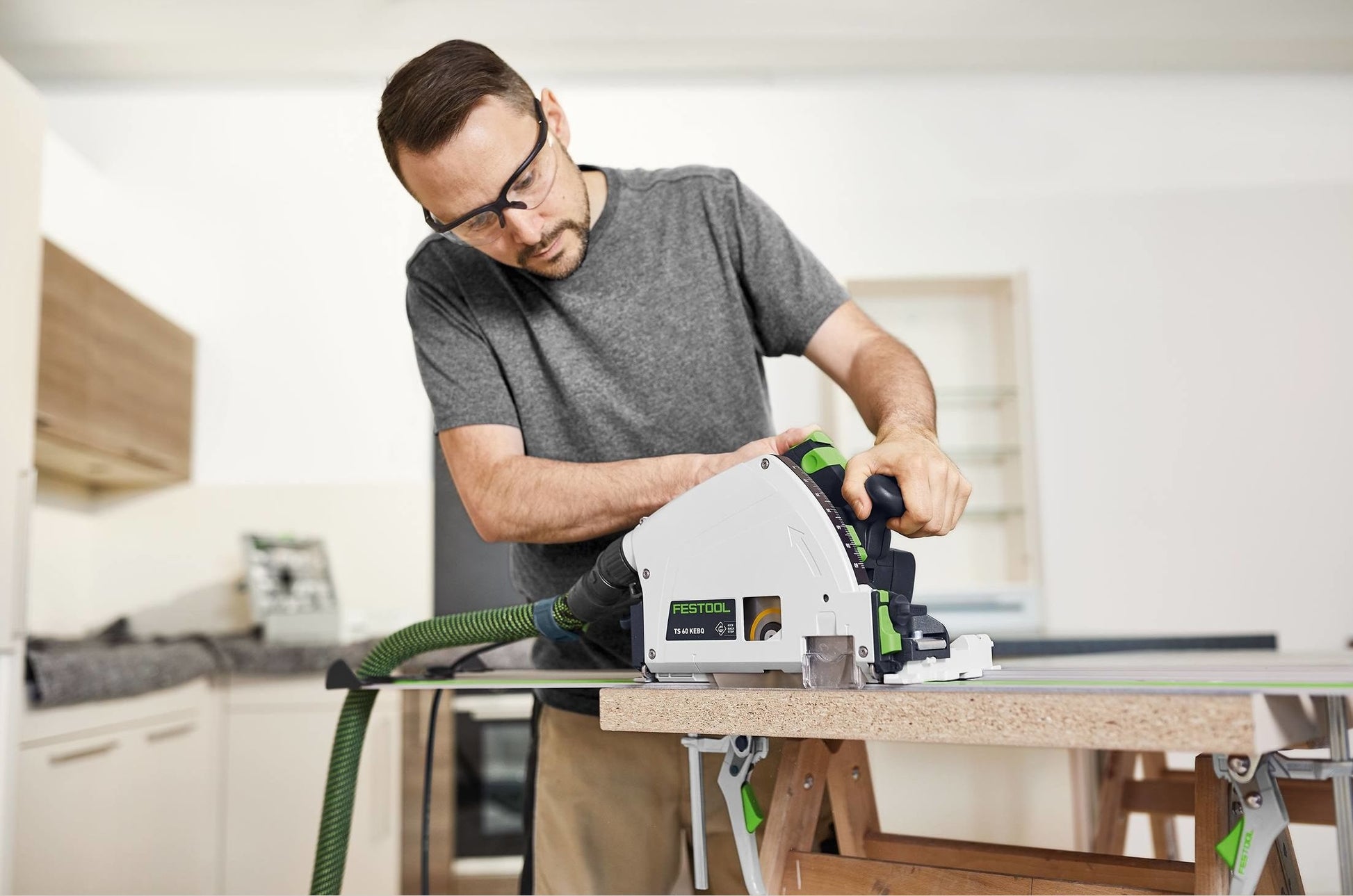 Man using a plunge cut track saw on wood panel in modern kitchen for home improvement tools and power saws.
