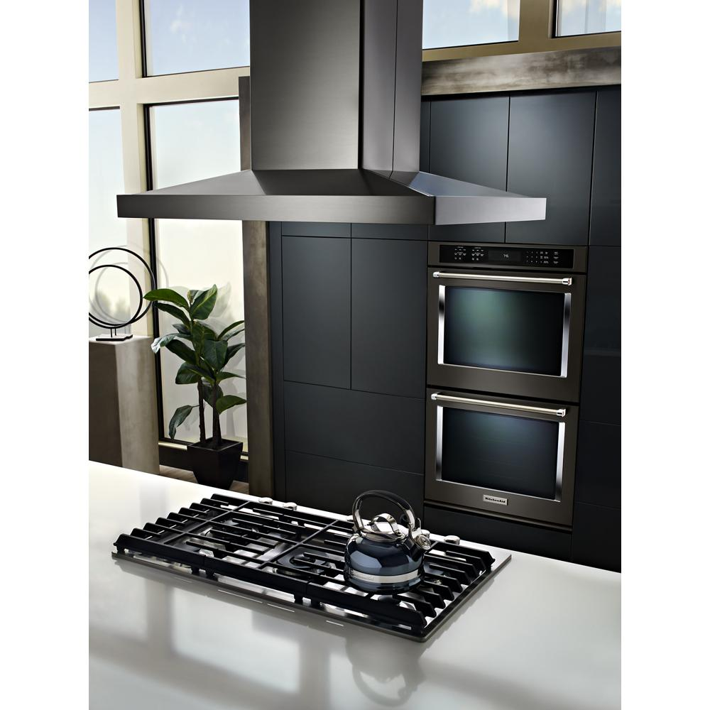 Contemporary kitchen featuring a black gas cooktop with kettle beneath a stainless steel range hood and double wall ovens