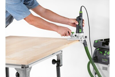 Person using Festool trim router with attached dust extraction on wooden board for precise home improvement tasks