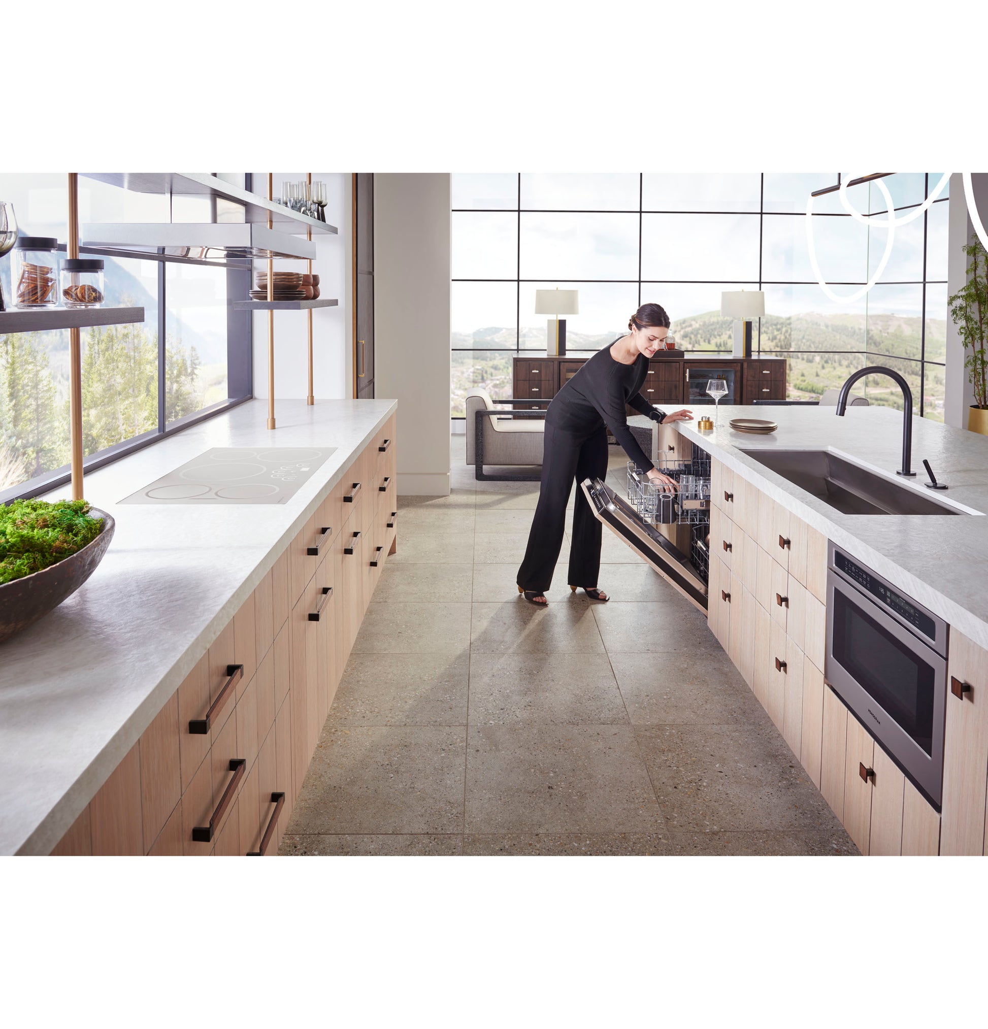 Modern kitchen with light wood cabinetry featuring built-in microwave drawer and a woman loading an open dishwasher