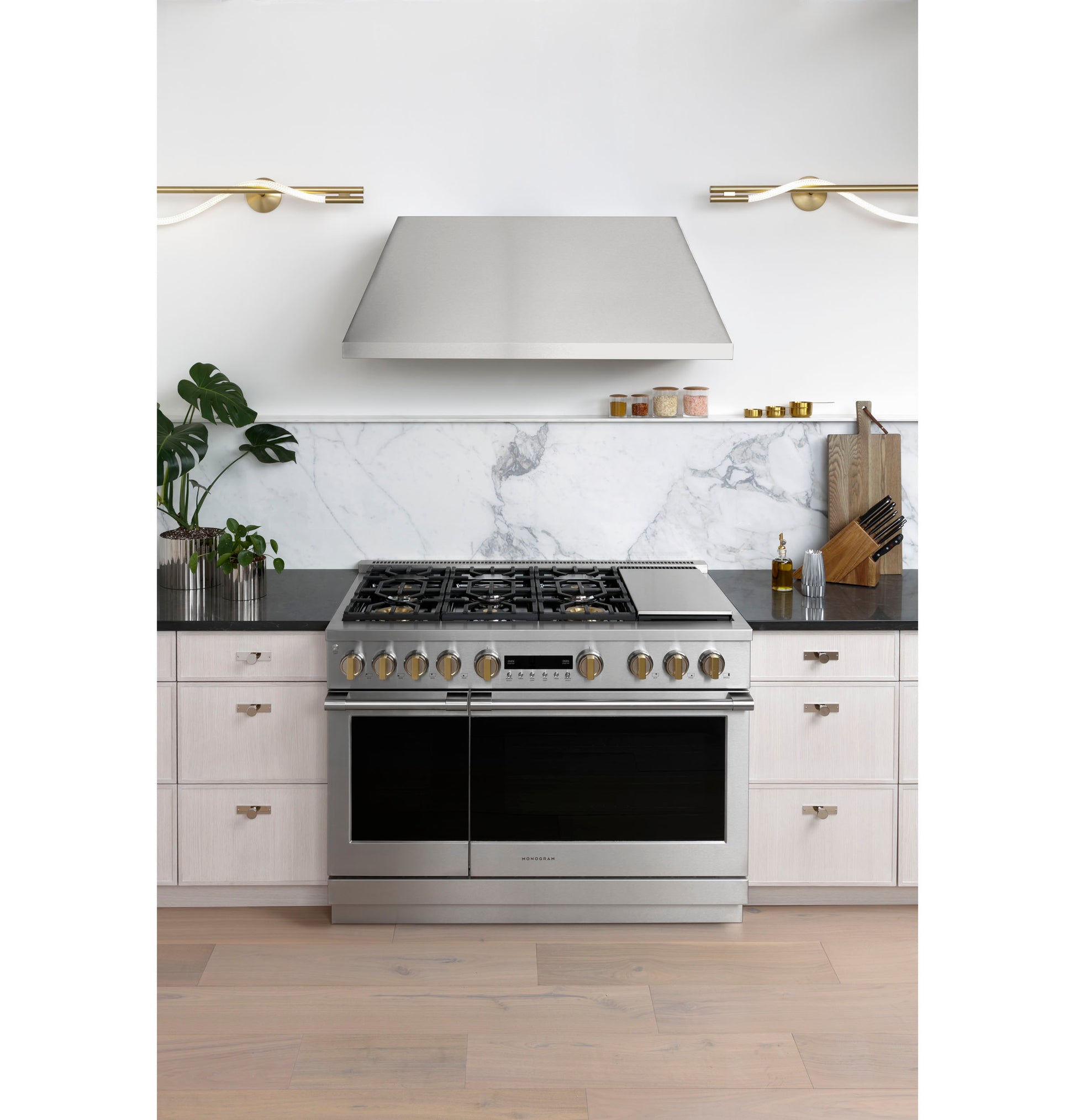 Stainless steel professional hood above gas range with marble backsplash in modern kitchen and home improvement appliances collection