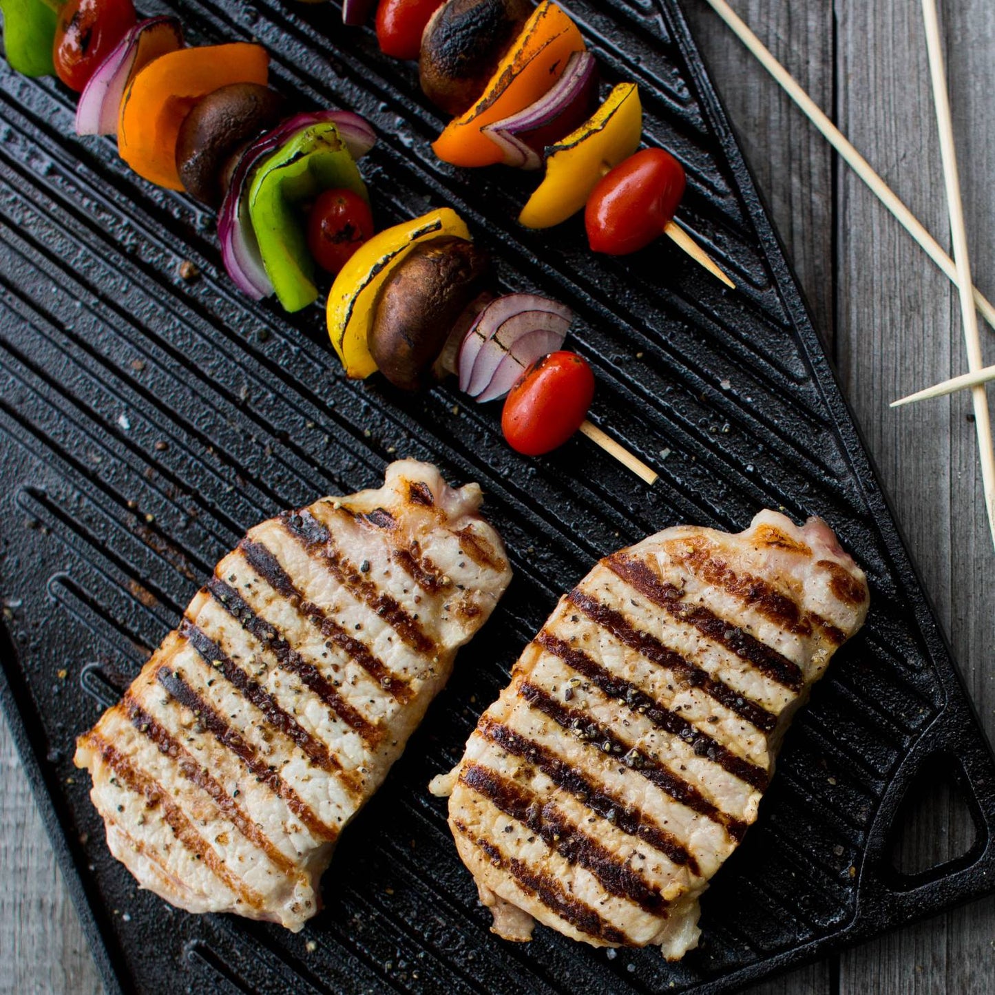 Double sided cast iron griddle with grilled chicken breasts and vegetable skewers for home cooking and tools use