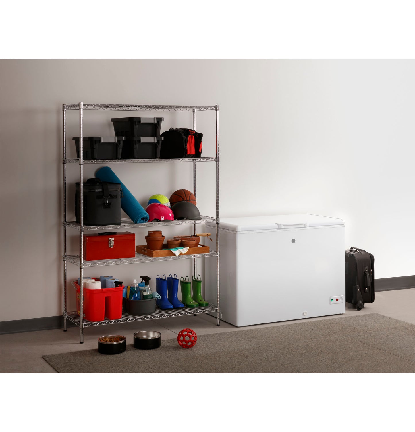 White manual defrost chest freezer in storage area beside metal shelving with sports, gardening, and cleaning supplies