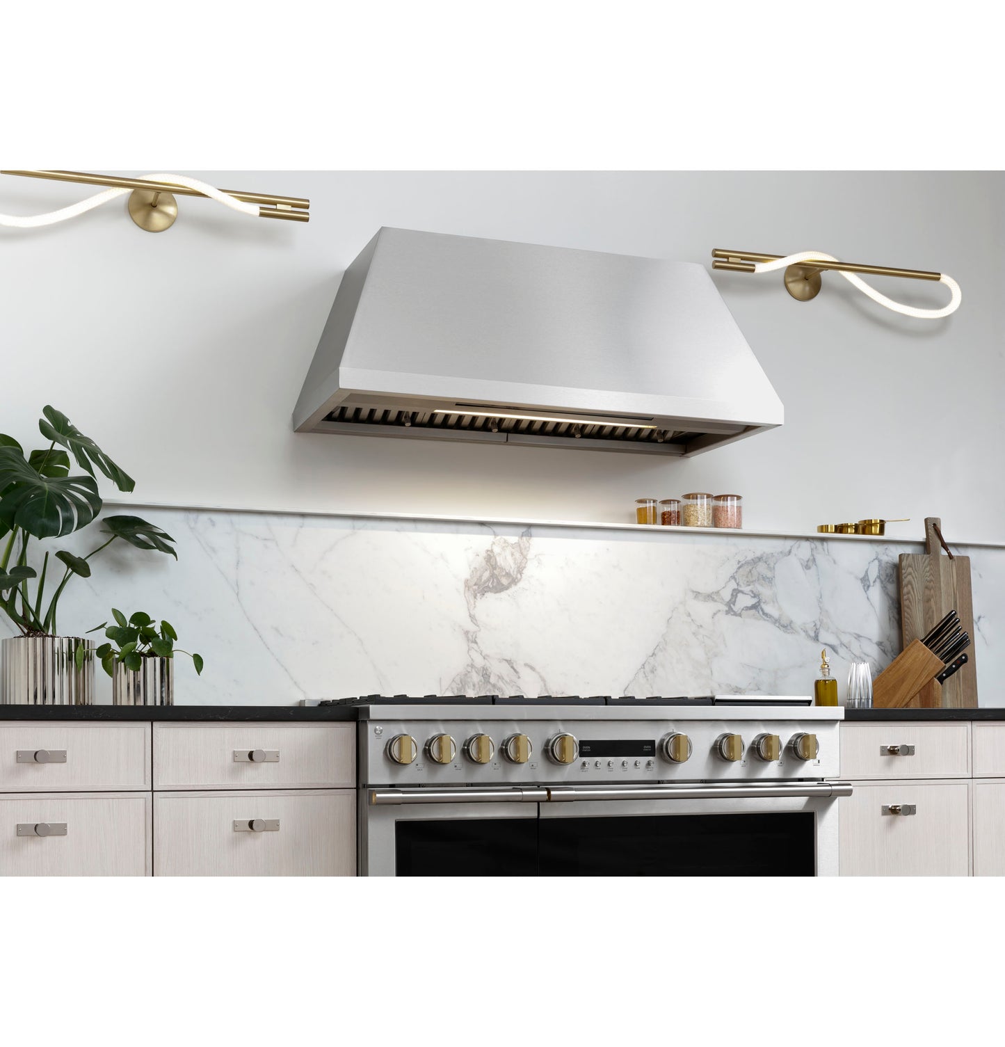 Stainless steel professional range hood mounted above a modern gas stove in a bright kitchen setting