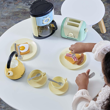 Child playing with pastel-colored toy kitchen appliances and breakfast accessories on white table