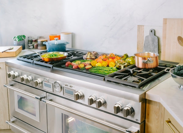 Stainless steel professional dual fuel range with food cooking on griddle and burners in modern kitchen setting