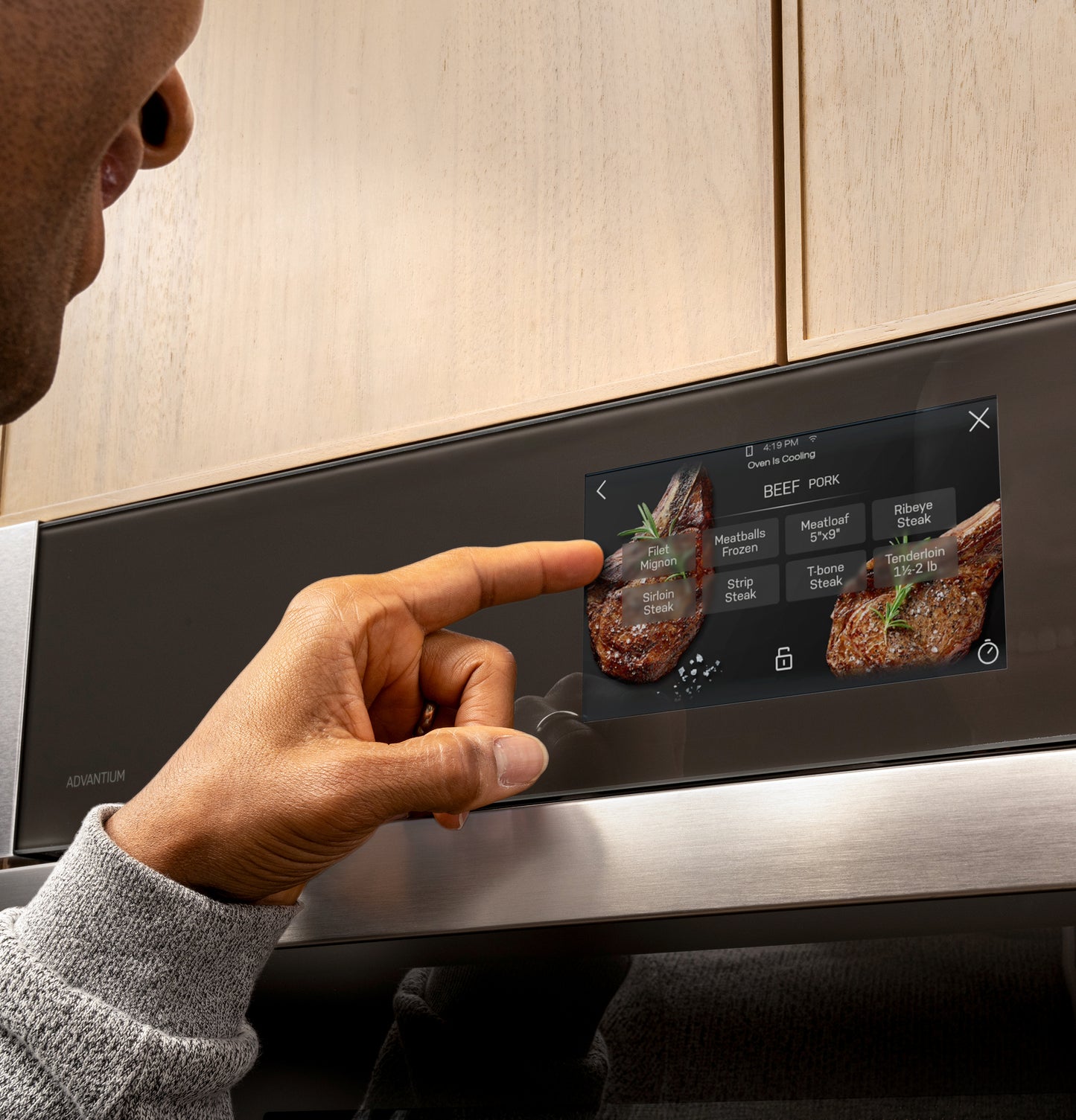 Finger selecting beef cooking options on digital touchscreen control panel of stainless steel wall oven in kitchen appliances