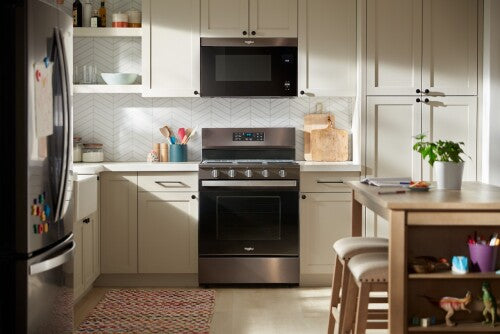 Modern kitchen with stainless steel gas range, white cabinetry, microwave, and organized countertop accessories