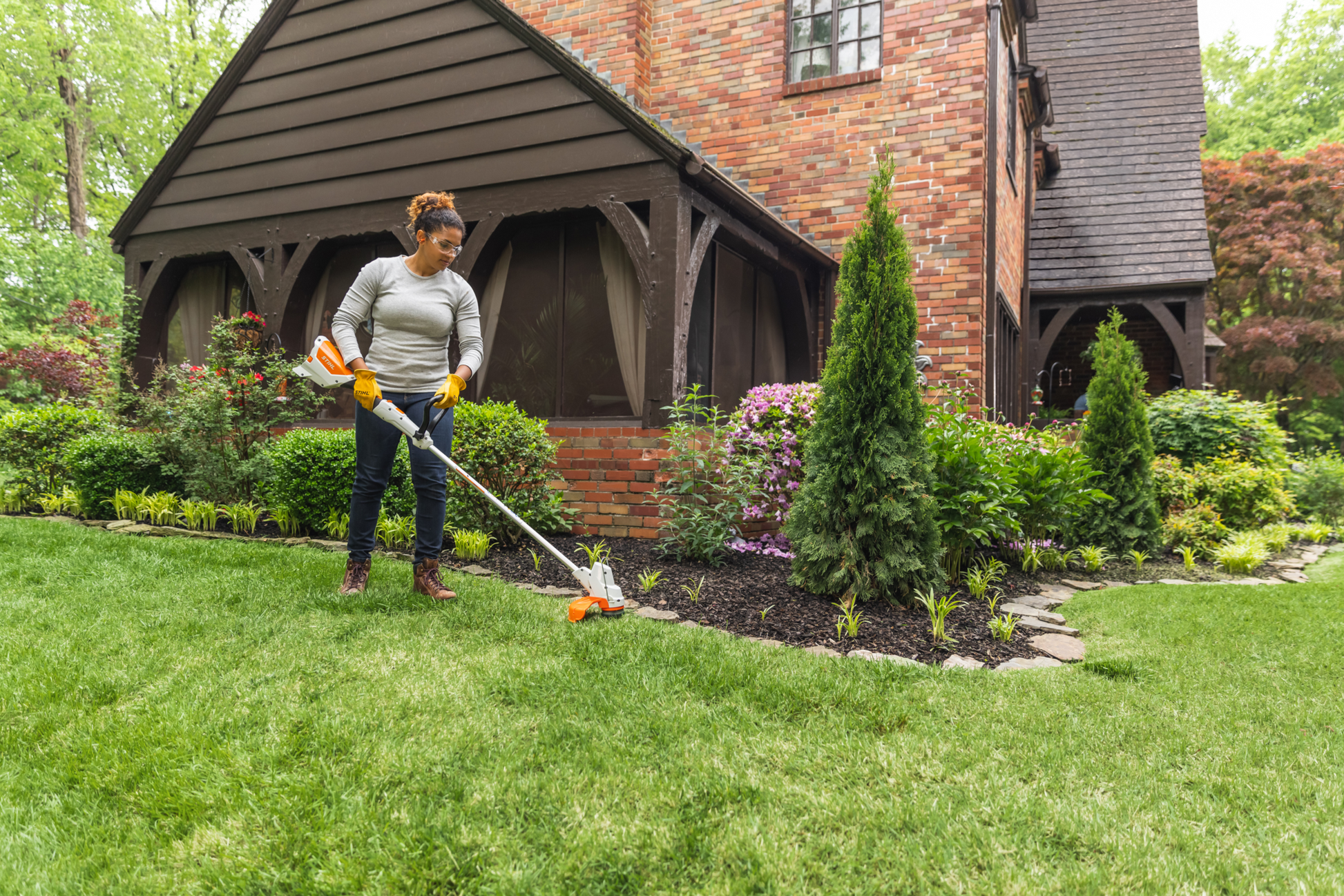 Person trimming grass along garden edge using lightweight orange and white battery-powered string trimmer for yard care tasks
