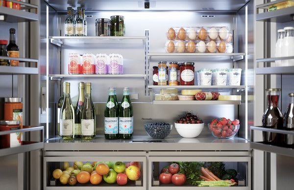 Open built-in stainless steel French door refrigerator with organized shelves holding beverages, fruit, eggs, and condiments
