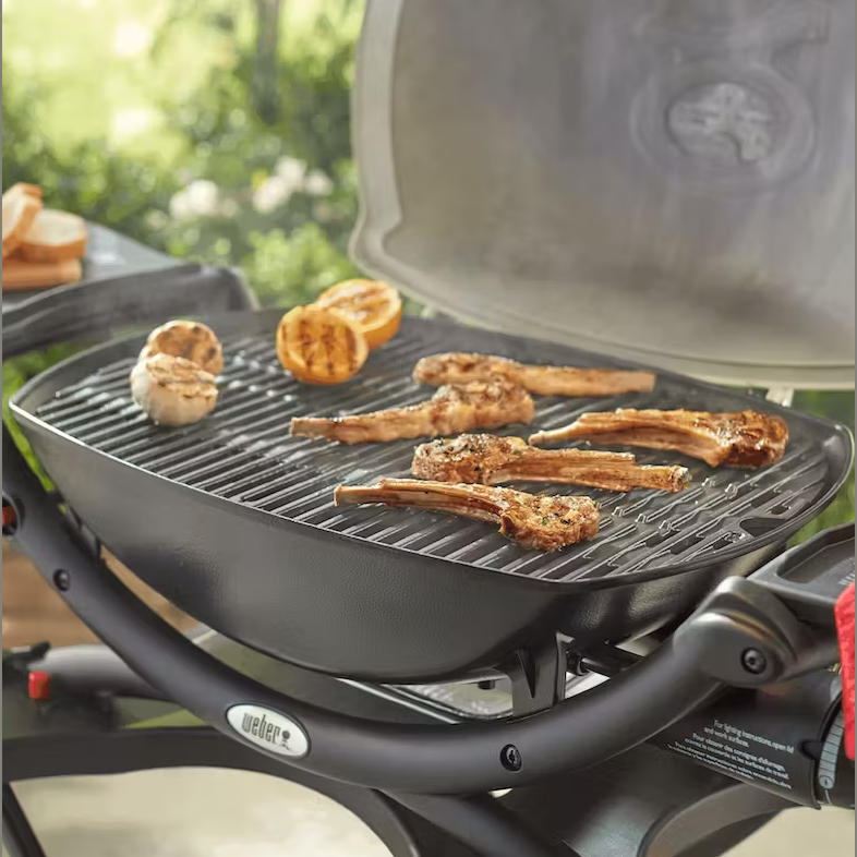 Cast iron cooking grate with grilled lamb chops and mushrooms on black outdoor Weber grill in garden setting