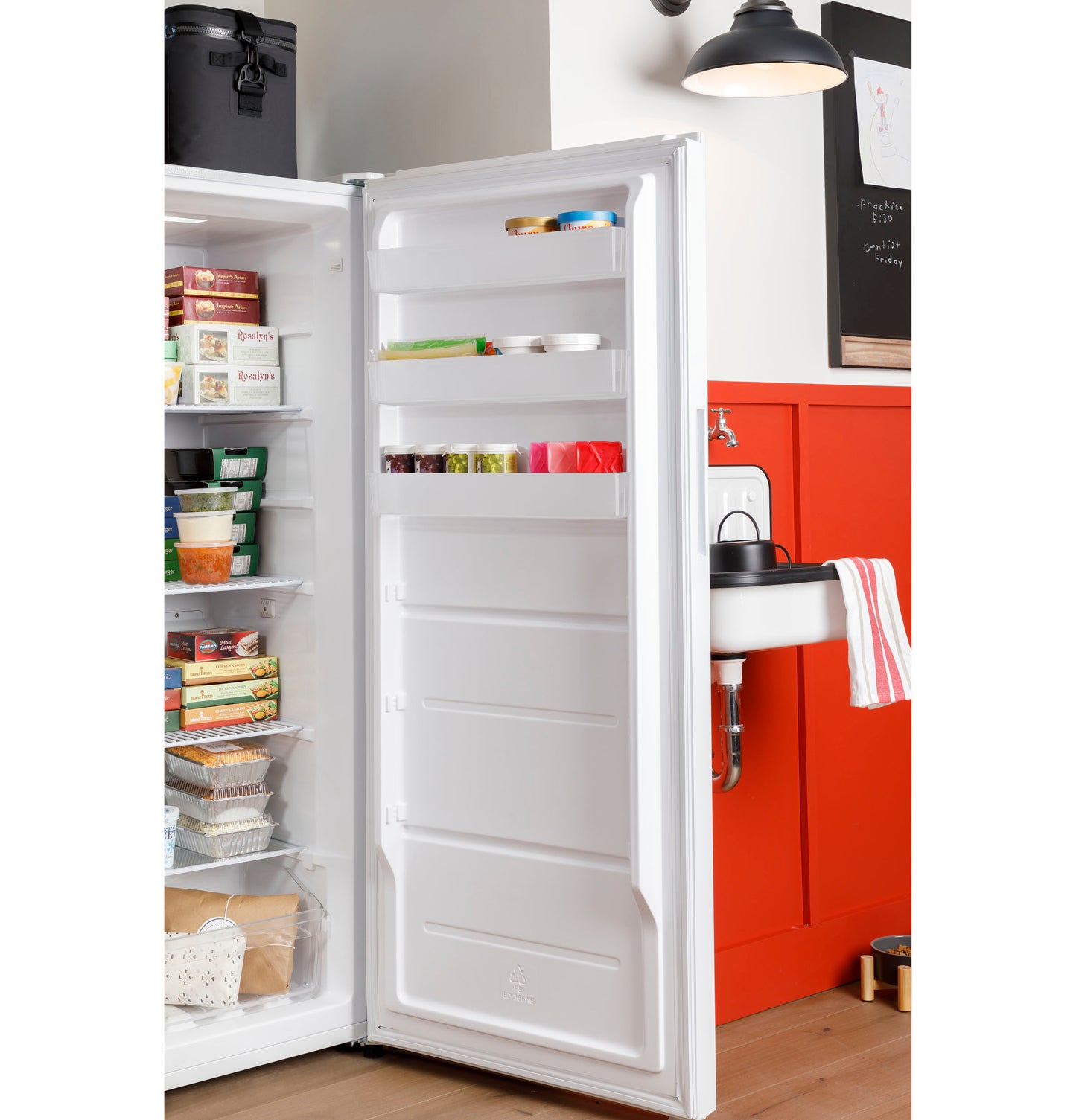 Open white upright freezer door showing shelves stocked with food containers in modern kitchen setting