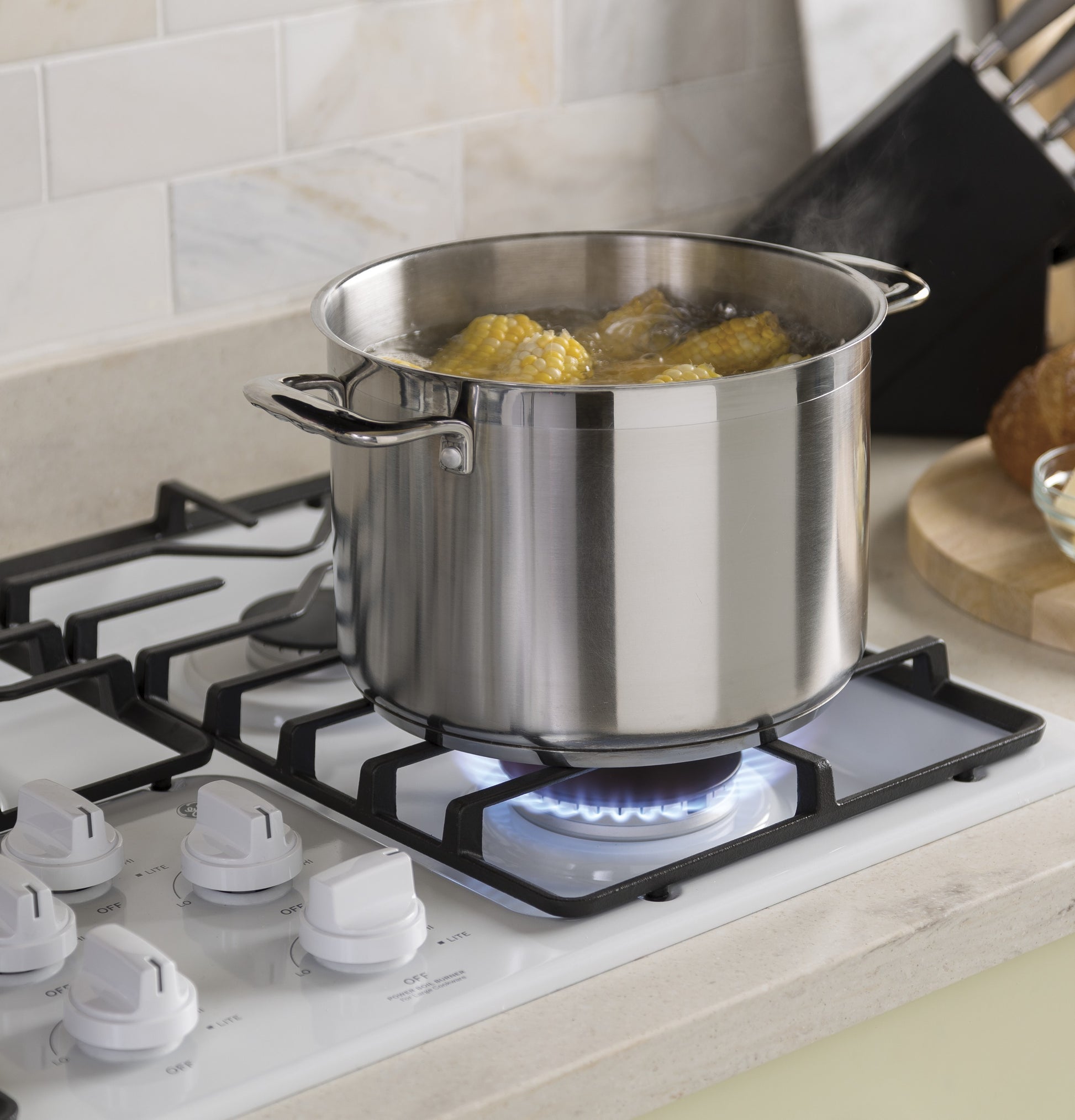 Stainless steel pot boiling corn on a lit burner of built-in gas cooktop in modern kitchen setting