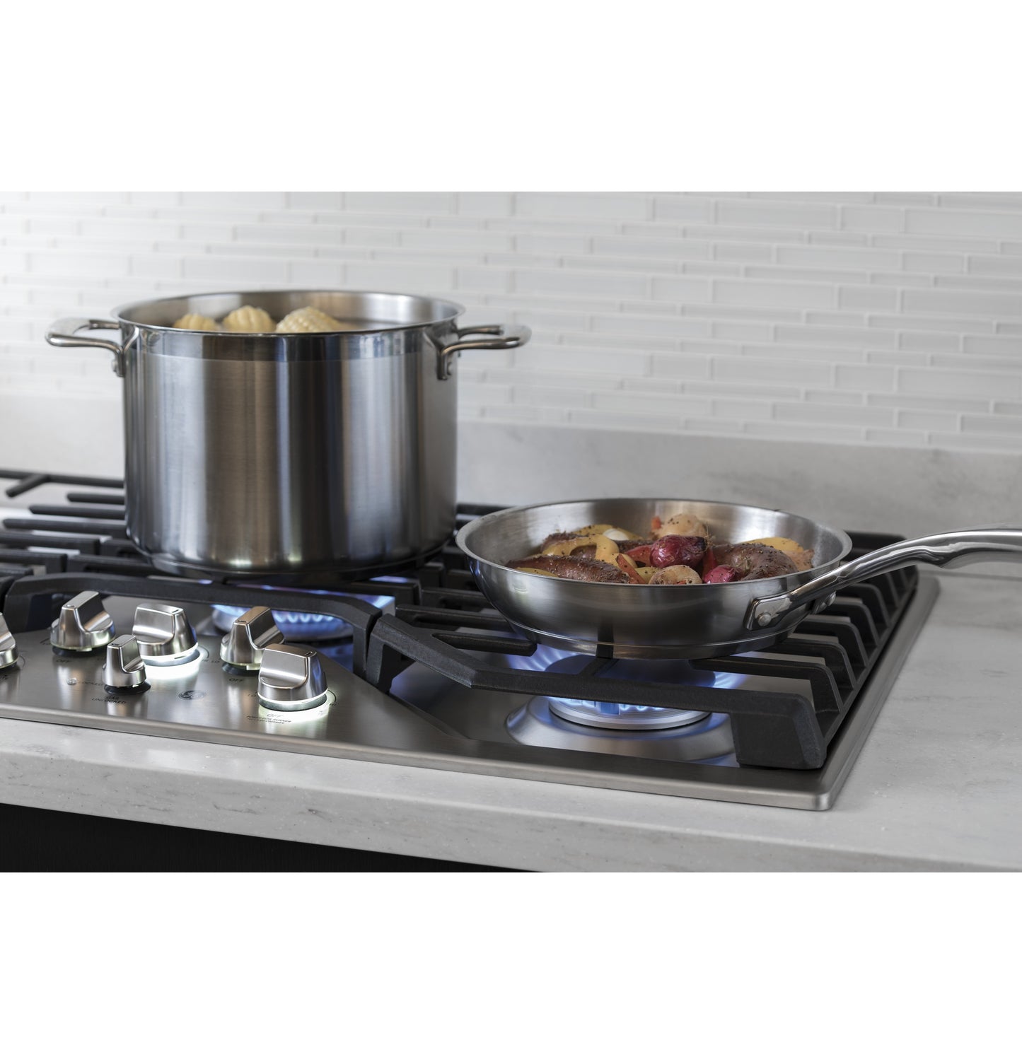 Stainless steel pot and skillet cooking on gas burners of a built-in cooktop in a modern kitchen setting