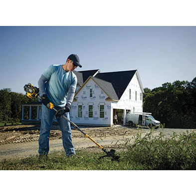 Man using cordless string trimmer to clear tall grass near new house under construction for home improvement tasks