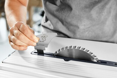 Hand adjusting angle gauge on a Festool cordless table saw blade for precise rip cuts in a workshop setting