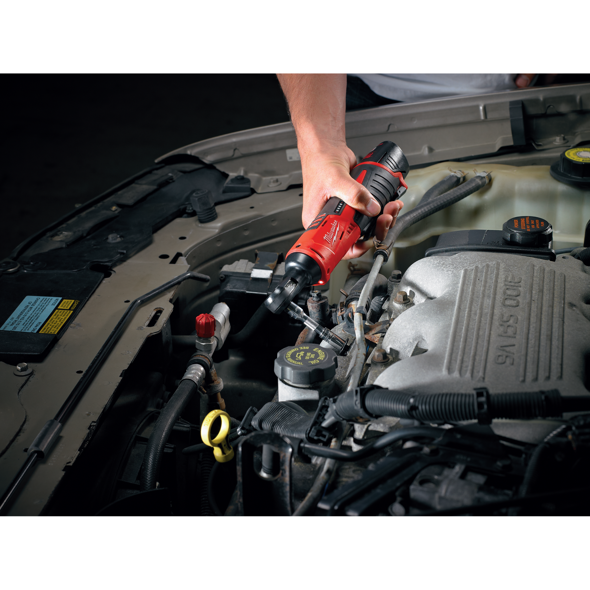 Hand operating Milwaukee M12™ cordless ratchet on car engine for tools and home improvement project