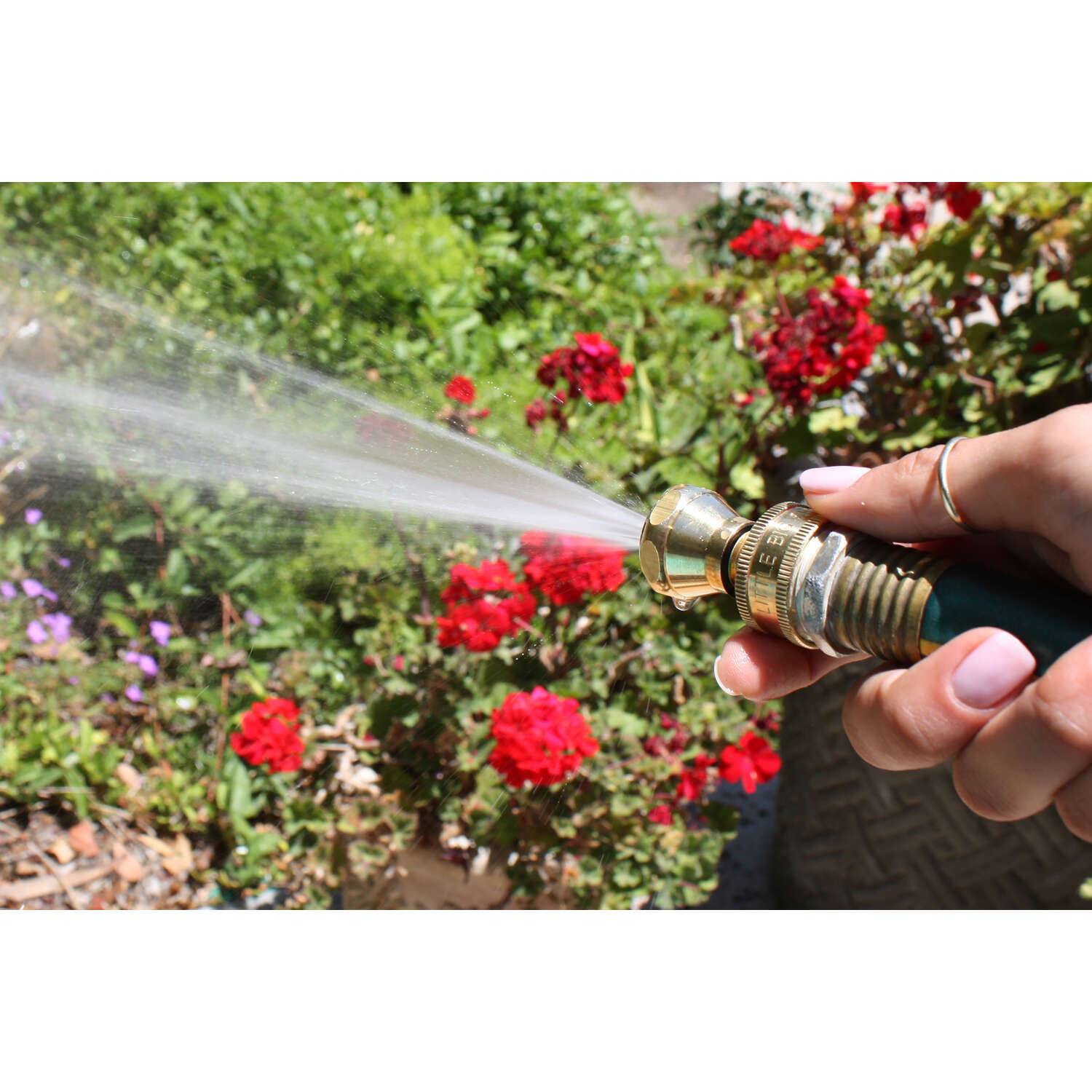 Hand holding brass twist nozzle spraying water on garden flowers for watering and irrigation tools collection
