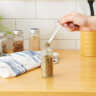 Hand holding polished stainless steel 1/4 teaspoon measuring spoon over a spice jar in kitchenware collections