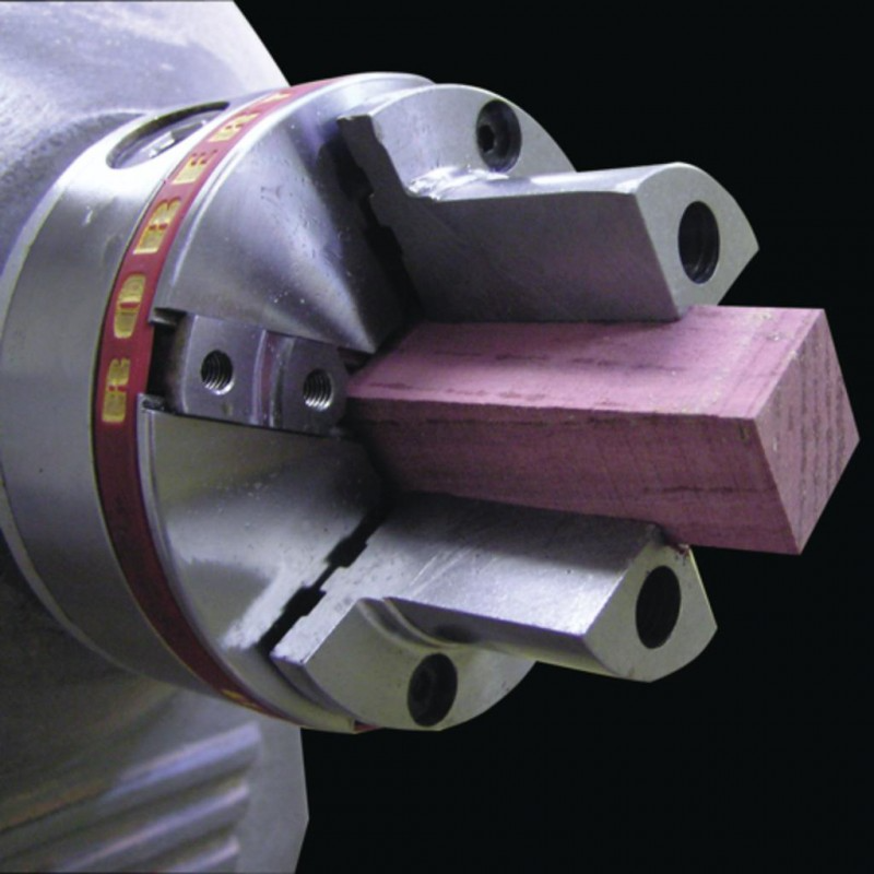 Metal pen jaws holding a rectangular wood piece in woodworking tool accessory for precision turning tasks