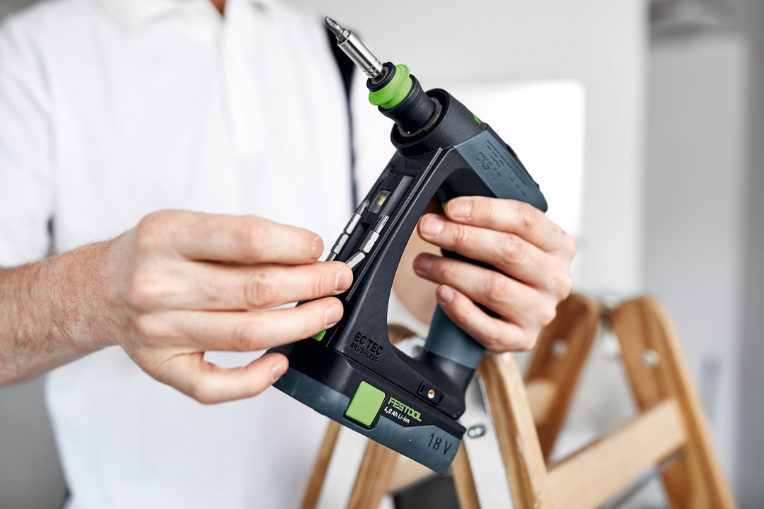 Person holding Festool cordless drill with screwdriver bit near wooden ladder for home improvement tasks
