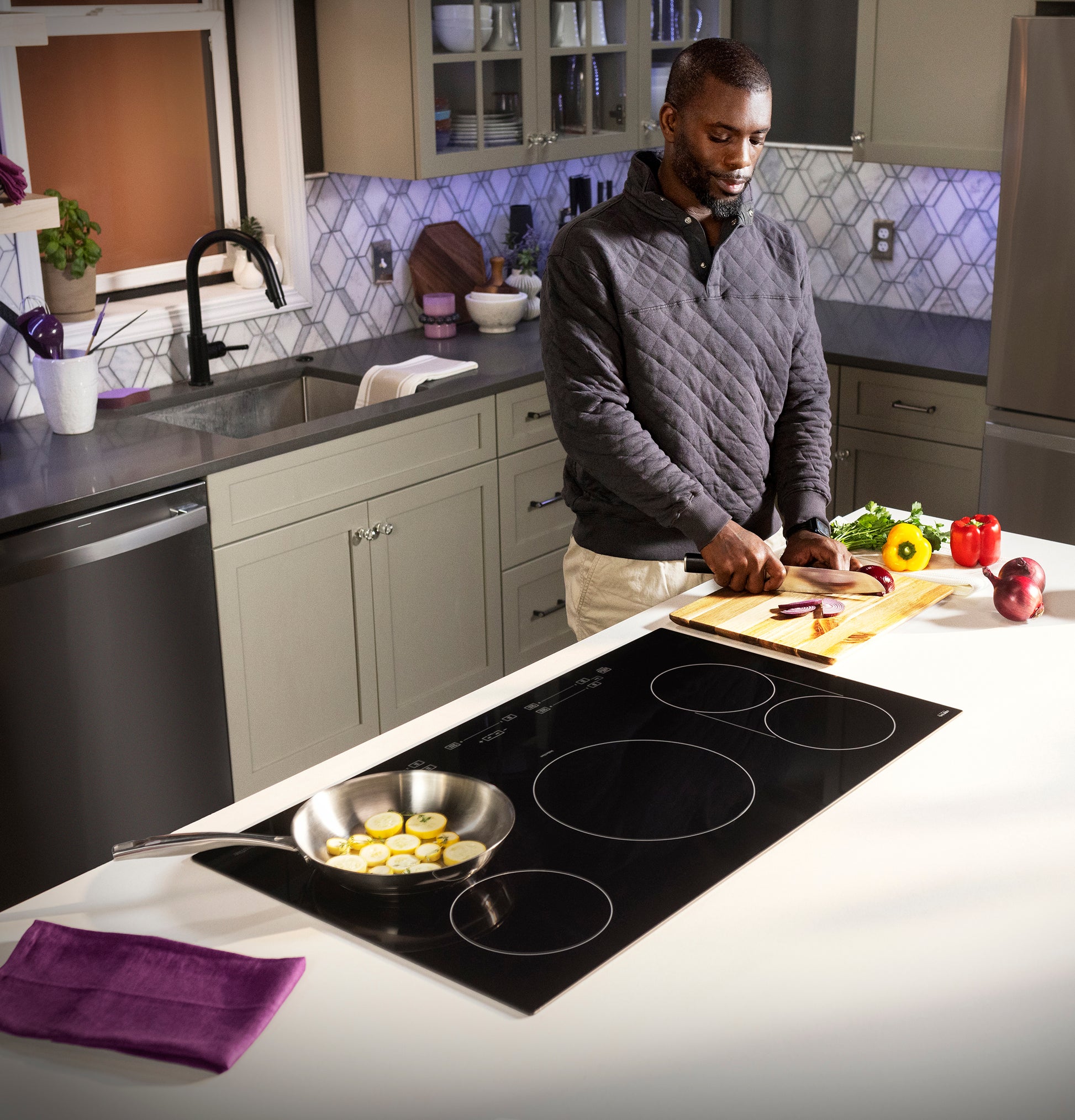 Man slicing vegetables on kitchen island with black touch control induction cooktop and stainless steel frying pan