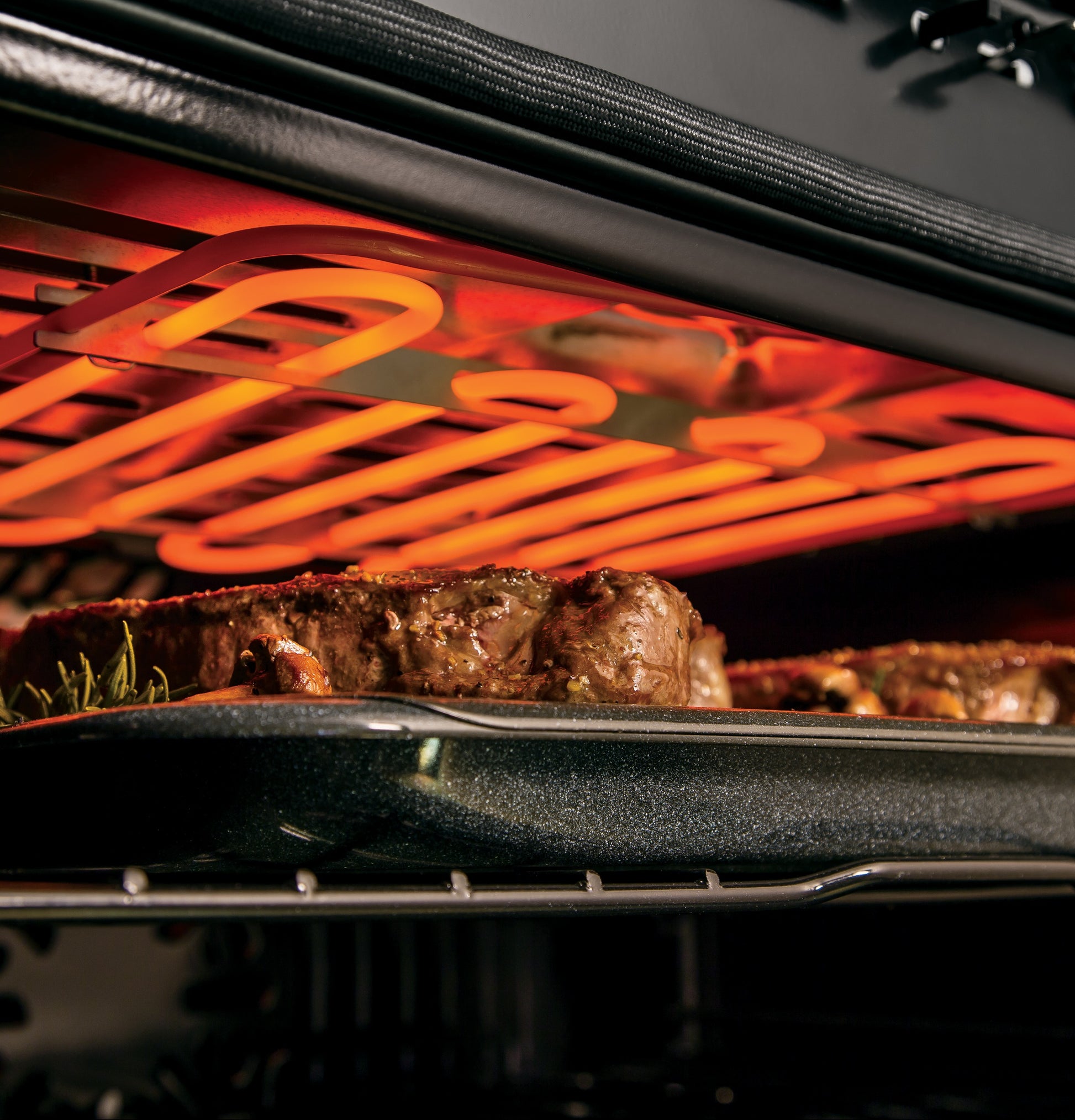 Close-up of meat roasting under the warming element inside a smart built-in convection wall oven rack in kitchen