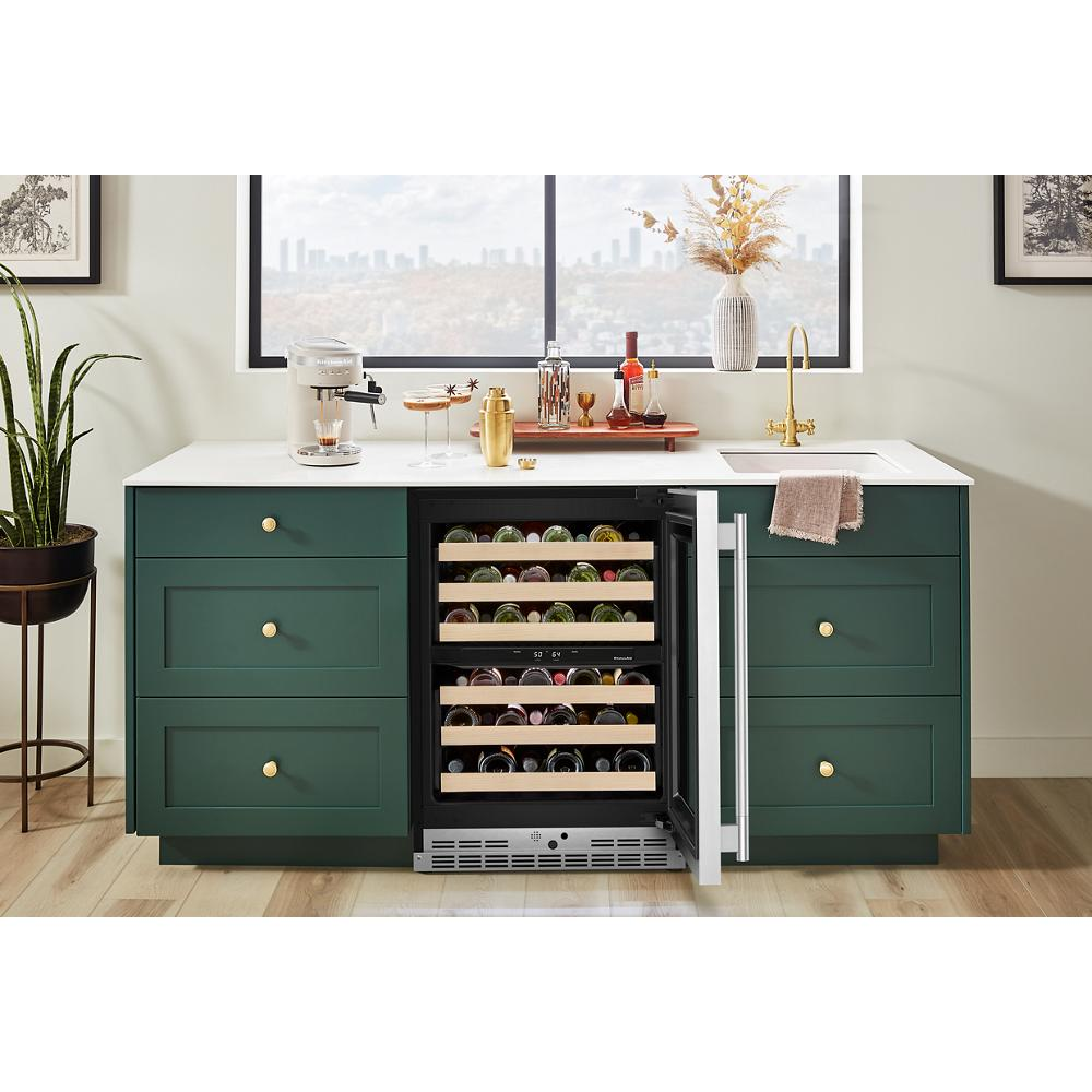 Kitchen bar area with green cabinets, white countertop, gold faucet, and open undercounter wine cellar with wood racks and bottles