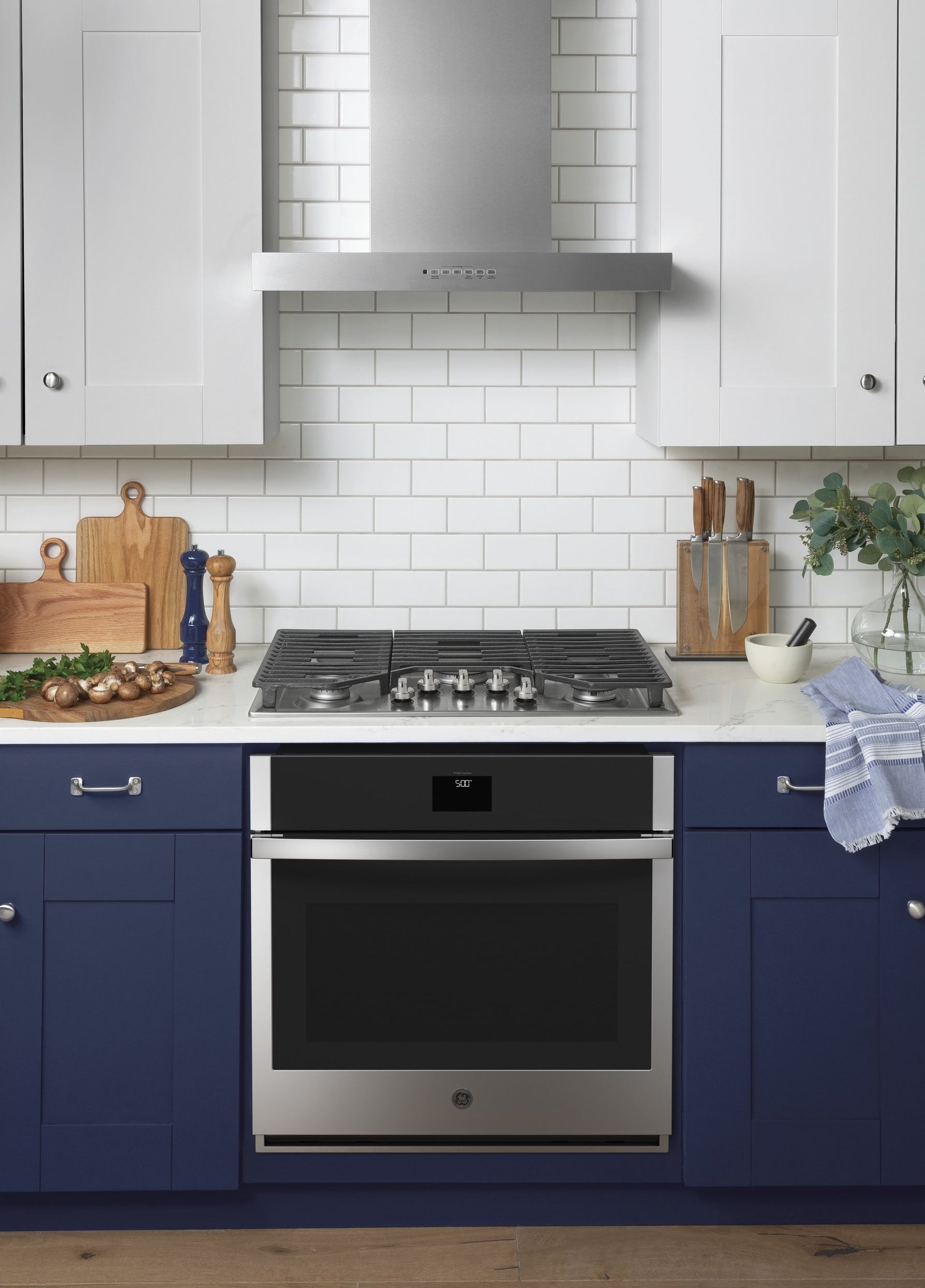 Stainless steel wall mount kitchen hood with touch controls above stainless gas cooktop and blue lower cabinetry