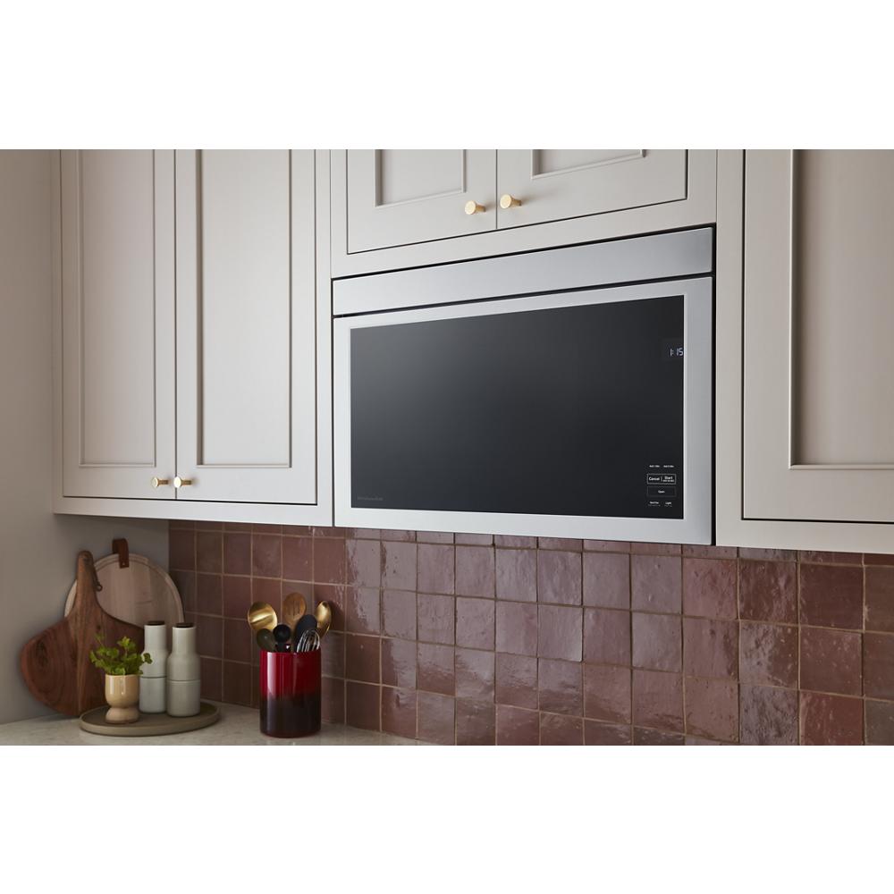 Black glass and stainless steel microwave built into cabinetry above a brown tiled backsplash in kitchenware setting