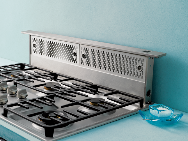Stainless steel downdraft vent installed behind gas cooktop in modern kitchen appliance setup