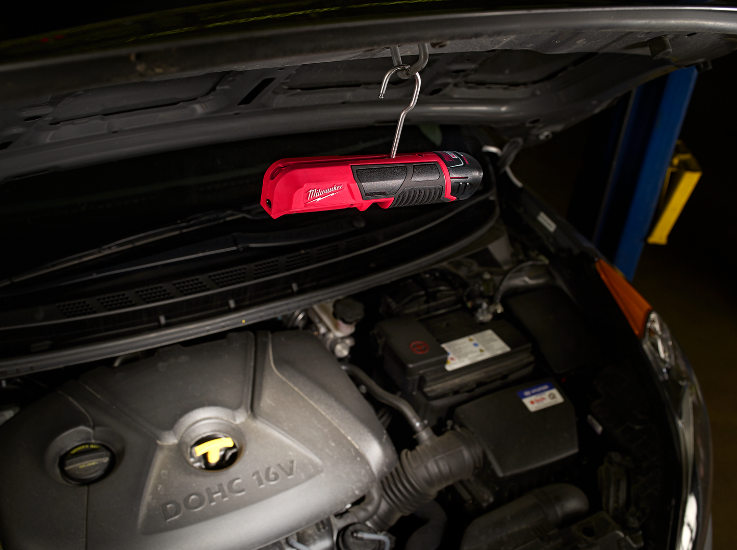 Compact red work light hanging from open car hood, illuminating engine compartment for home improvement tasks