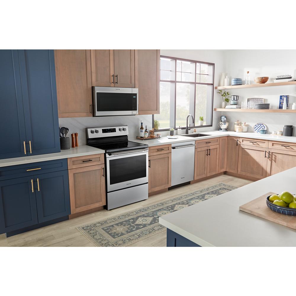 Kitchen with stainless steel electric range and microwave surrounded by blue and wood-tone cabinetry and light flooring