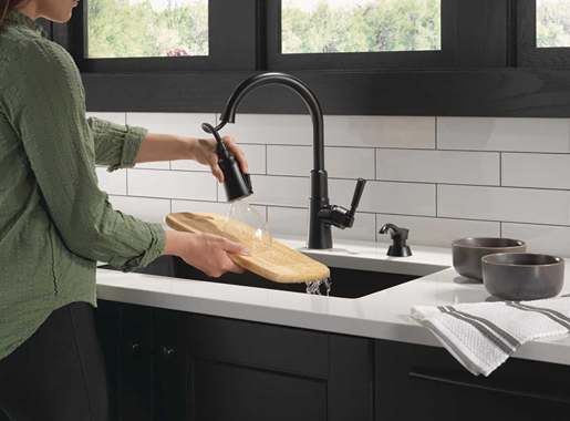 Matte black single-handle pull-down kitchen faucet with soap dispenser in modern kitchen setting cleaning wooden tray