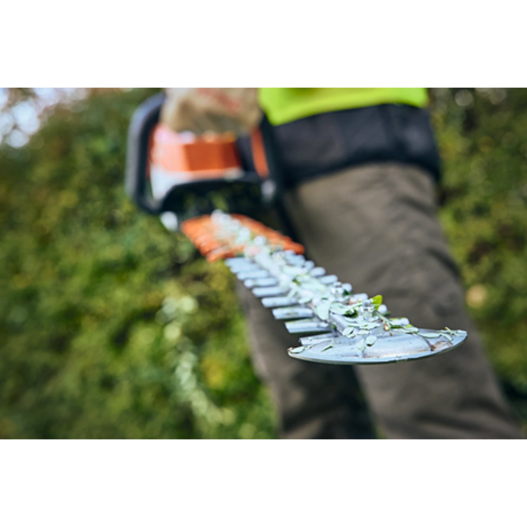 Close-up of an orange and white hedge trimmer blade cutting green shrubbery for tools and home improvement use