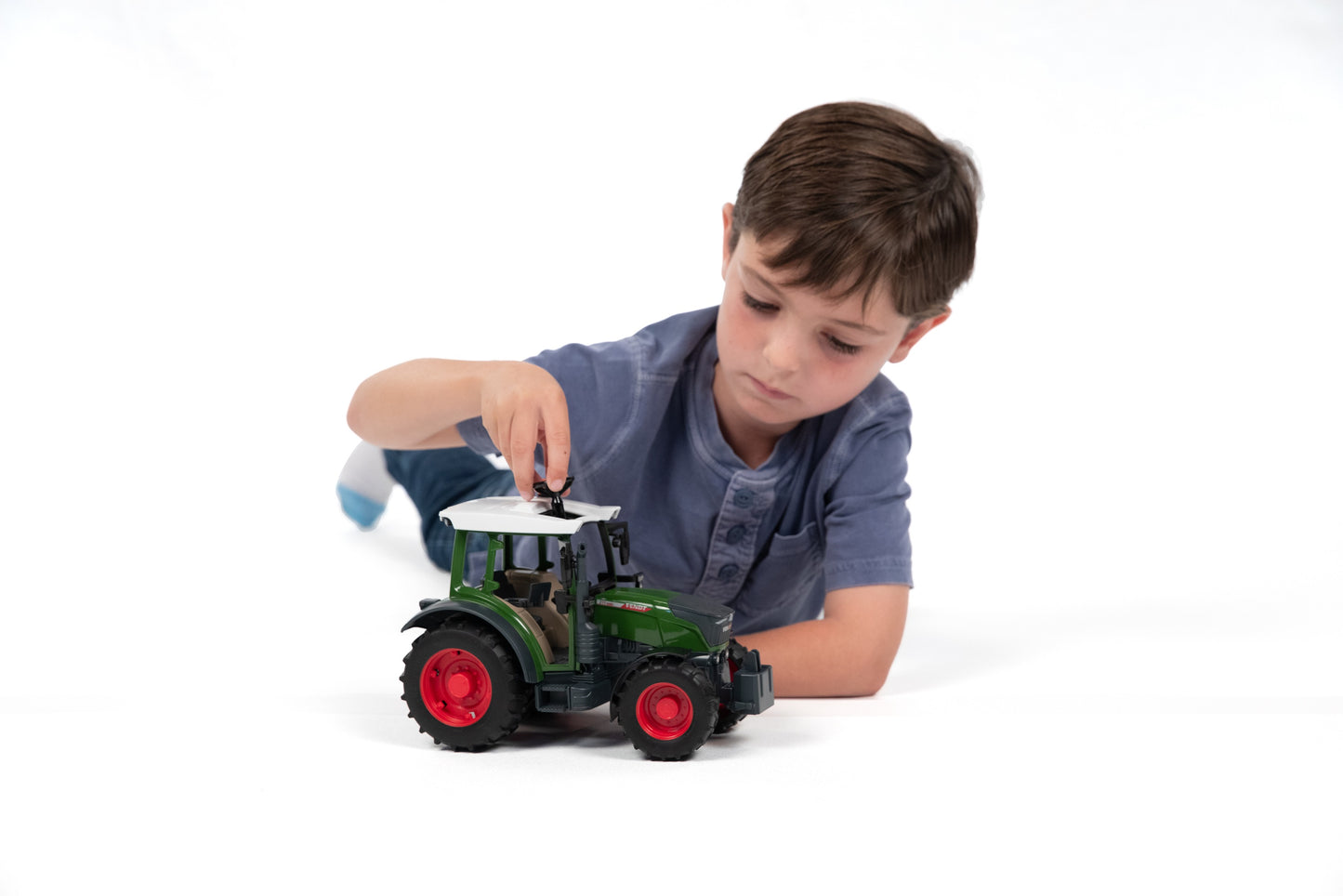 Boy focused on adjusting the roof of a green and red Bruder tractor model for tools and home improvement fans